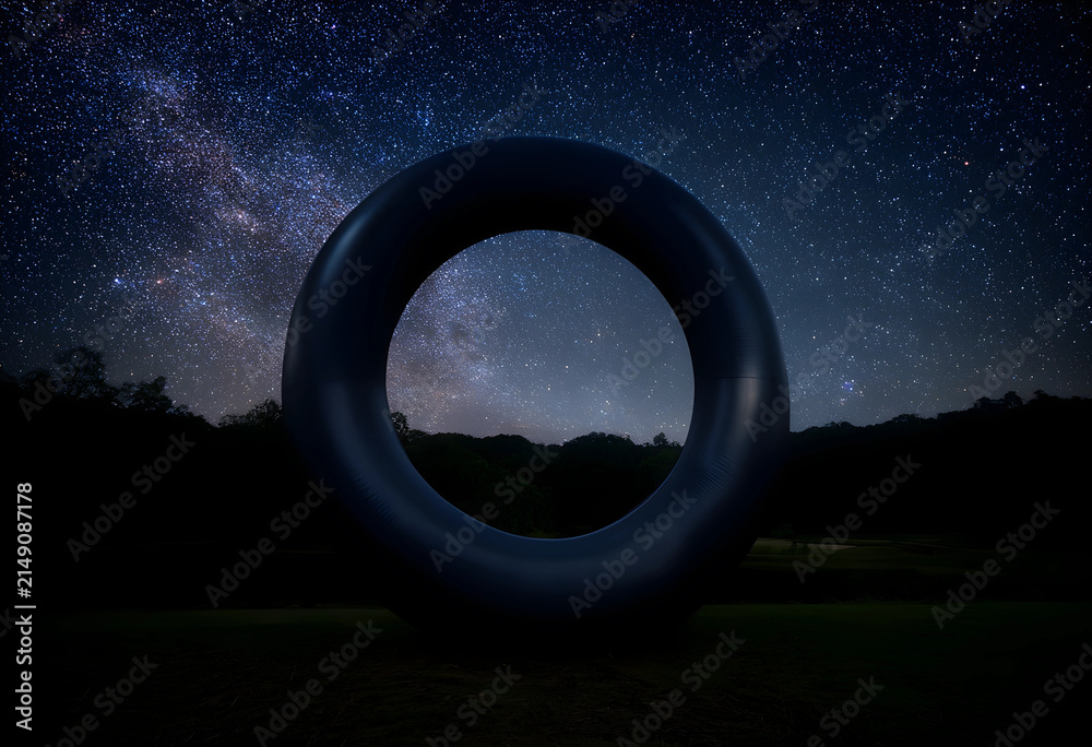 Obraz premium Dark inflatable ring standing on grass under a starry night sky with the milky way visible through the opening