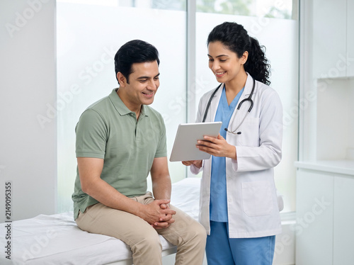 Indian female doctor consulting middle aged man with tablet in modern clinic for preventive healthcare patient education insurance and medical services