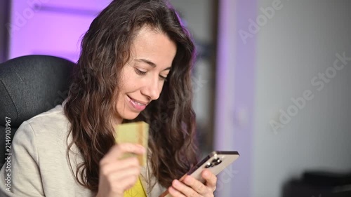 Happy woman entering credit card details on her smartphone for online shopping and payment in a modern office at night