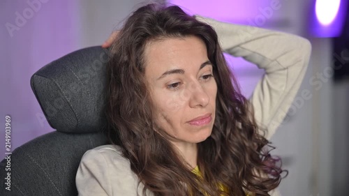 Thoughtful woman with curly hair sitting in a gaming chair thinking and reflecting about her life feeling sad and pensive