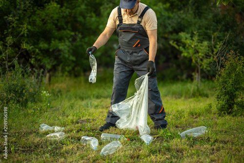 Photography A garbage collector is collecting plastic bottles from the ground in a park
