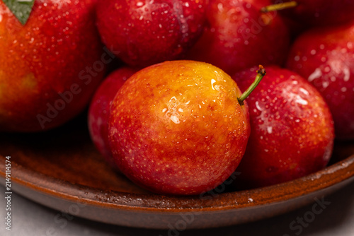 Fresh red and yellow plums with water drops in bowl