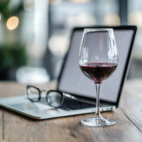 Sophisticated red wine glass placed on a table beside a laptop and reading glasses in a contemporary environment