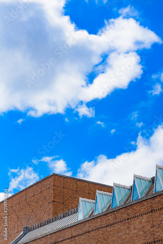 Brown brick wall with a distinctive triangular glass panel roof under a bright sky filled with soft, scattered clouds.