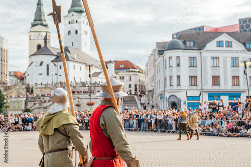 Medieval Festival Battle Reenactment In City Square With Crowd And Historical Buildings Backdrop During Bright Summer Festival Event Outdoors Exhibition Display Setup Historic Public Performance Show