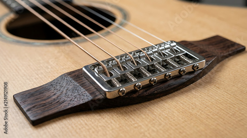Detailed close-up of an acoustic guitar bridge showcasing its intricate metal hardware and wooden components