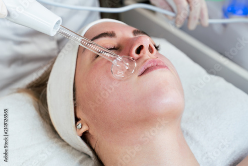 Cosmetologist using frequency darsonval device for skin rejuvenation, acne treatment, and anti-aging therapy in a modern medical spa.