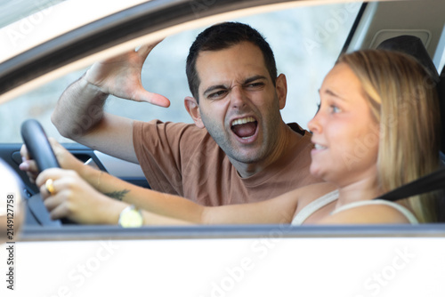 A young couple arguing heatedly inside a car; the man is shouting with his hand raised while the woman appears surprised and upset. An example of tense couple conflict and road rage