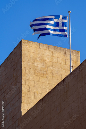 Greek flag flies over a stone building under a clear blue sky during the day