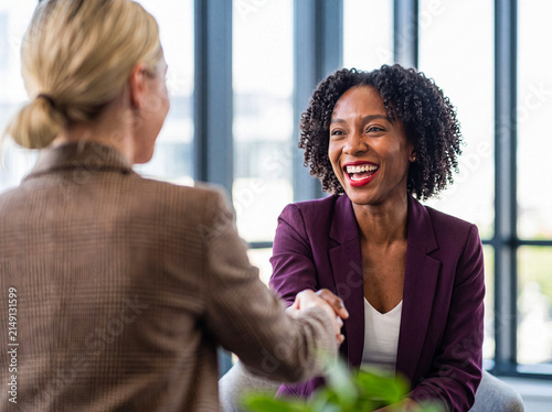 Photography Happy young African American businesswoman laughing and shaking hands with a colleague in a bright modern office