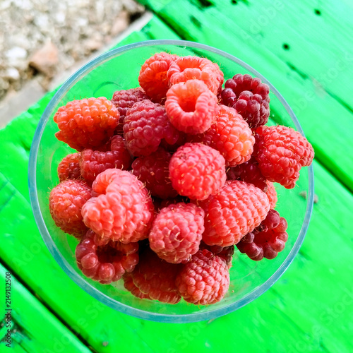 Fresh raspberries in glass bowl on green garden table