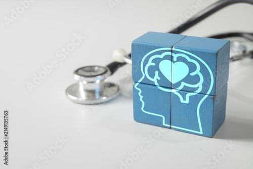 Mental health diagnosis and psychological care concept. Blue wooden blocks with a digital human head, brain, and heart graphic next to a stethoscope on a white background.