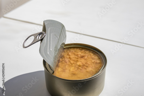 Canvas Print Open metal tin can filled with canned meat on a white table in direct sunlight