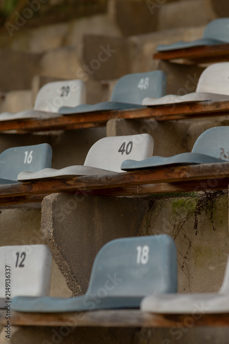фотографія Rows of worn plastic seats with white painted numbers mounted on aged concrete bleachers
