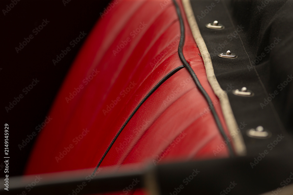 Obraz premium Tight view of a red leather automobile seat featuring vertical quilting, black piping trim, and adjacent black fabric with chrome snap fasteners. Warm