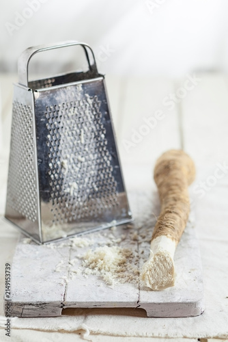 Grated horseraddish and grater on kitchen board