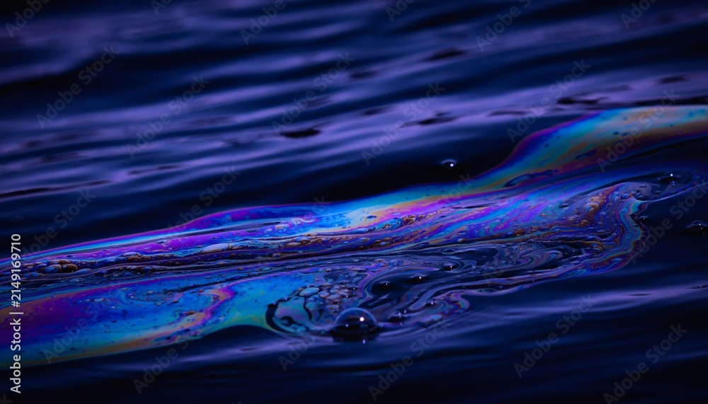 Fototapeta premium Iridescent oil slick floating on dark rippled water
