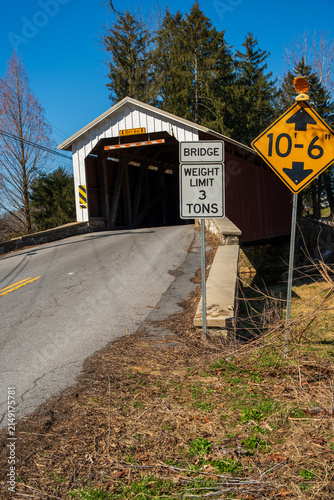 Old covered bridge located on a rural road surrounded by trees in the daytime