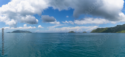 Fotografie Wide panoramic view of deep blue sea surrounded by lush green islands under a dy