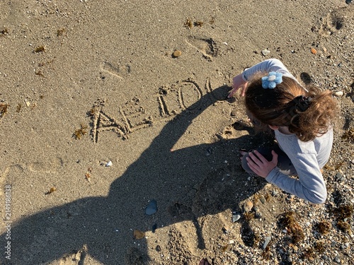 Obraz na plátne Little girl writing letters and vowels on beach sand during summer vacation