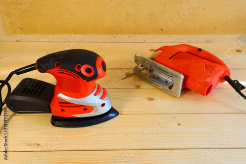 Canvas Print Orange-and-black sander stands beside open-framed saw on light wood planks