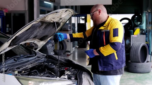 Focused mechanic checking car oil level with concentrated expression in vehicle repair workshop maintaining professional maintenance work
