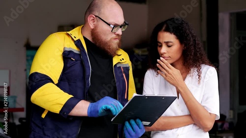 Focused man and woman looking document workshop with serious expression, mechanic paperwork car repair professional, clipboard advice attentive
