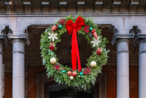 Large traditional Christmas wreath with a big red bow hanging on an old architectural stone building facade with columns