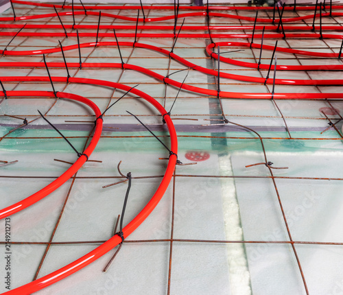 Red underfloor heating pipes installed on metal mesh grid on concrete floor, black zip ties secure pipes
