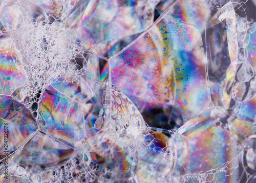 Macro abstract of shimmering bubble membranes with colorful interference patterns and fine lacy foam clusters.