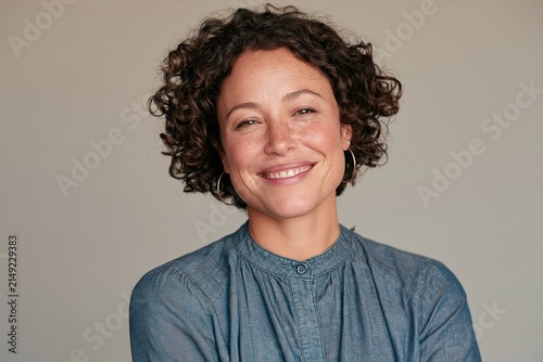Smiling woman with curly hair and freckles wearing a blue denim shirt