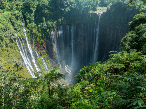 The breathtaking view of Tumpak Sewu Waterfall, surrounded by lush tropical forests in East Java, Indonesia.