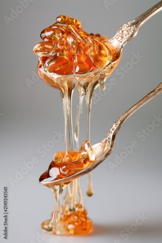 Golden honey drips slowly from a spoon in a glossy, viscous stream. Natural sweetness, wholesome ingredients, breakfast food.