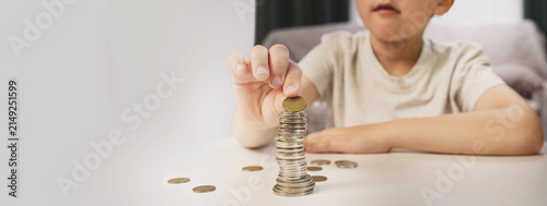 A little boy counts coins on a living room table. Financial scarcity training. Kids and money. Savings, personal finance. copy space banner