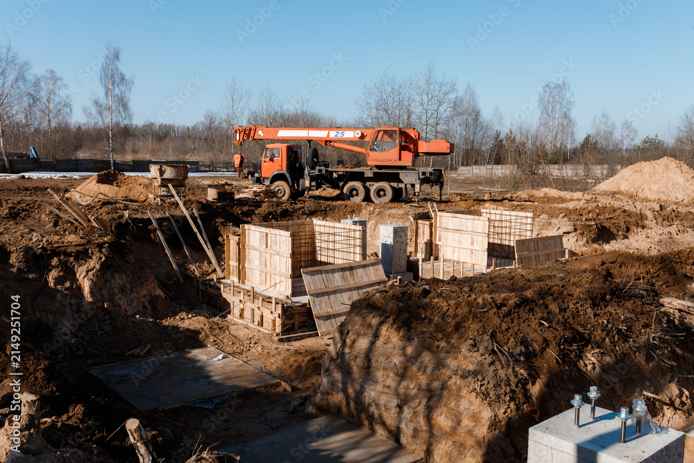 Fototapeta premium Orange truck mounted mobile crane near foundation formwork pit at industrial construction site building infrastructure engineering project background heavy machinery ground nobody clear blue sky