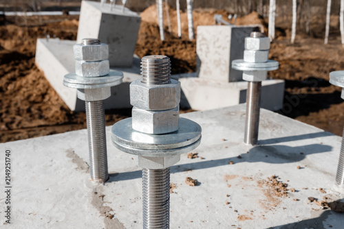 Steel anchor bolts with hex nuts and washers embedded in concrete foundation block close up at industrial construction site building infrastructure engineering project background nobody