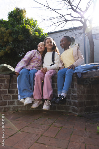 African American youth females sitting together on brick wall in school courtyard with backpacks