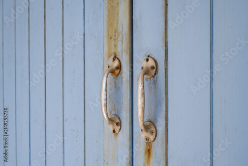 Fotografía Weathered metal door handles on pale blue painted wood with rust staining and la