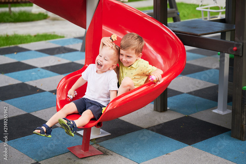 Foto Two boys sliding together on red playground slide, laughing and holding toys, jo