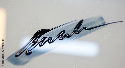 Abstract black liquid stroke on a white reflective surface creating an elegant flowing shape resembling a modern artistic signature or ink drip