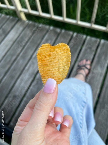 Photography Hand holding ridged heart-shaped potato chip on wooden deck outdoor