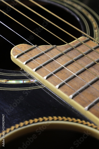 Close‑up of an acoustic guitar showing the glossy dark body, decorative sound hole, and wooden fretboard with metal frets