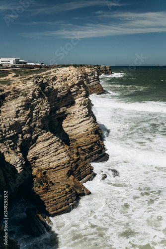 Fotografie Close up view of dramatic layered rock formations dropping into the churning ocean water in Peniche, Portugal