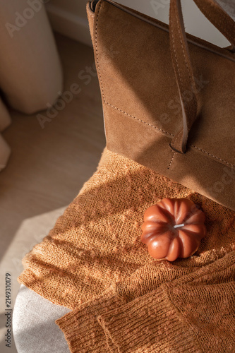 Fashion autumn aesthetic still life, terracotta knitted clothing on chair, caramel sueded bag, pumpkin candle with soft natural sunlight, lifestyle home interior