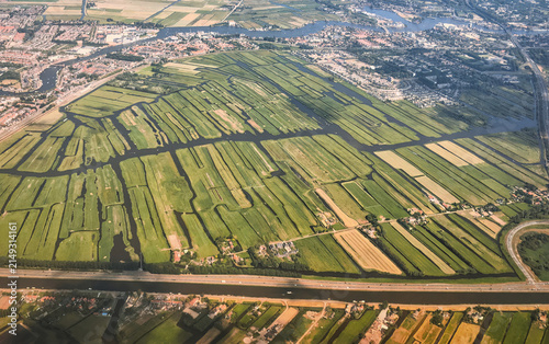Aerial view of a Dutch agricultural landscape featuring green polder fields crisscrossed by dark water canals and a suburban settlement, showcasing intricate land reclamation patterns. Alphen aan den