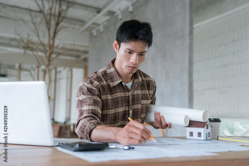 Fototapeta premium Architect working at a laptop with architectural blueprints in a modern studio, representing building design, construction planning, engineering, and professional project development.