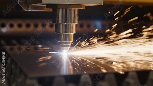 Macro shot of an industrial CNC laser cutting machine processing a metal sheet with bright flying sparks.