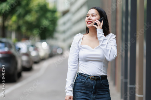 Canvastavla Young woman confidently walking on a city street, communicating on her smartphon
