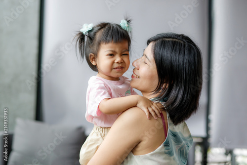 Smiling mother holding her playful little daughter at home, capturing love, family bonding, happiness, warmth, childhood, and natural lifestyle in soft daylight, Asian Thai people