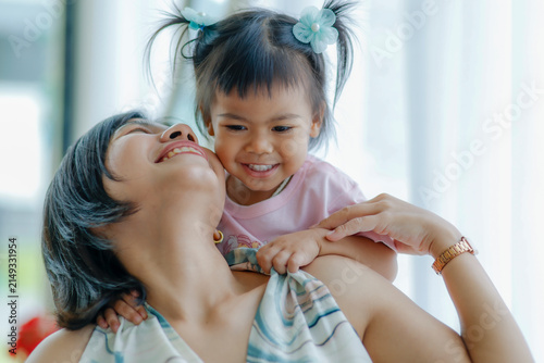 Happy mother carrying her little daughter on her shoulders, sharing joyful smiles that express love, family bonding, warmth, care, trust, and precious moments at home, Asian Thai people
